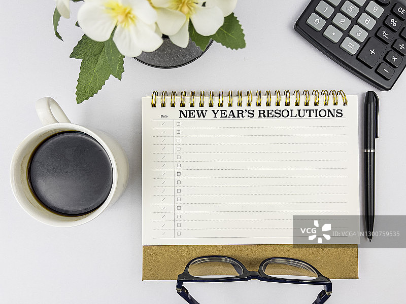 记事本上的新年计划文本，搭配笔、眼镜、咖啡、花和计算器。商业、金融、经济和行动计划概念背景。白色背景。图片素材