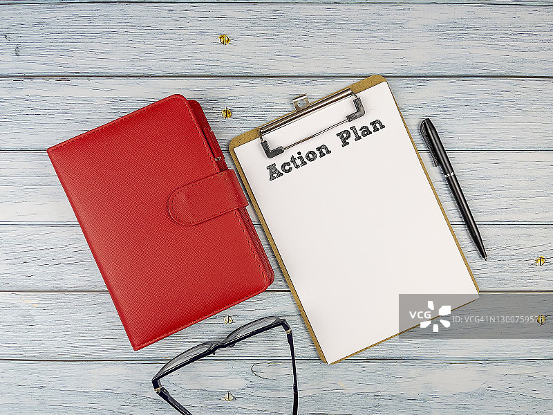 记事本上的行动计划文本，配有红色日记、笔、眼镜和计算器，位于木桌顶部。商业、金融、经济和行动计划概念和背景。图片素材