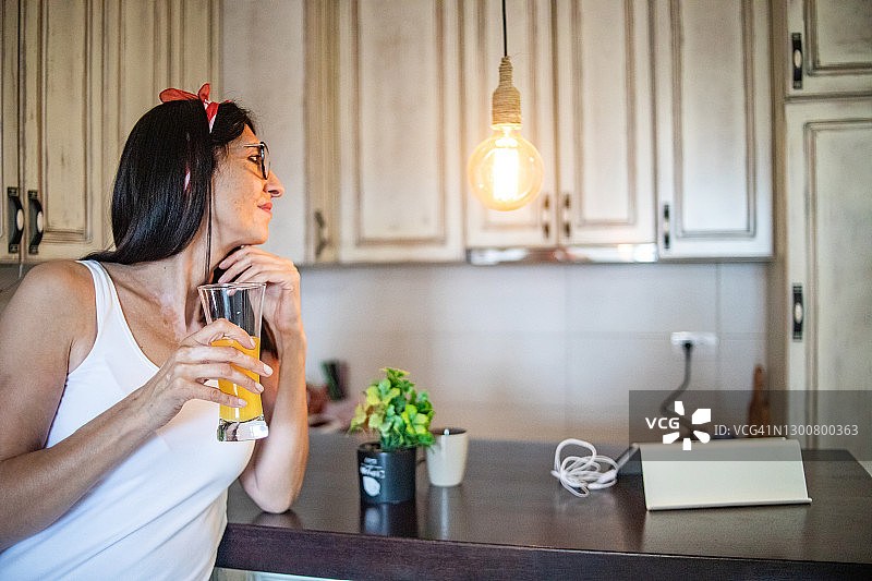 微笑的黑发中年妇女在厨房喝早咖啡，通过平板电脑进行视频通话图片素材