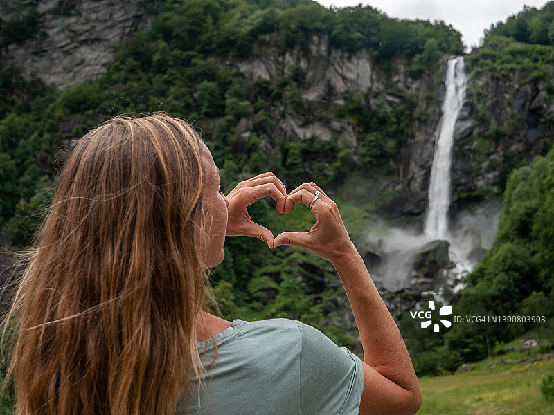 女人热爱自然，在瀑布前用手比心图片素材