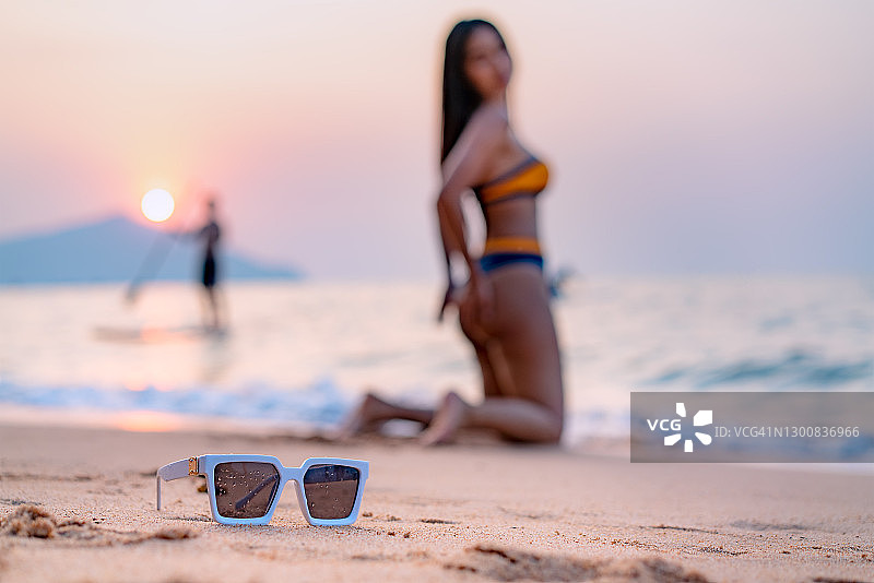 女人戴着太阳镜坐在海滩上，夏季特写图片素材