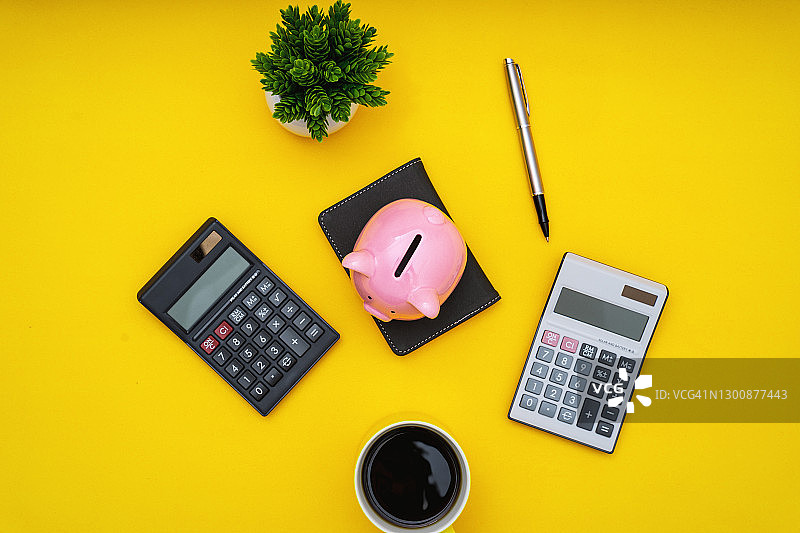 黄色桌子上带计算器的储蓄罐俯视图图片素材