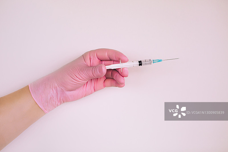 戴粉色手套的医生在白色背景上拿着装有冠状病毒疫苗的小注射器图片素材
