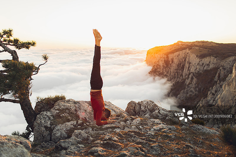 男人在山中练习头倒立哈他瑜伽，欣赏日落时分壮丽的云海景观图片素材