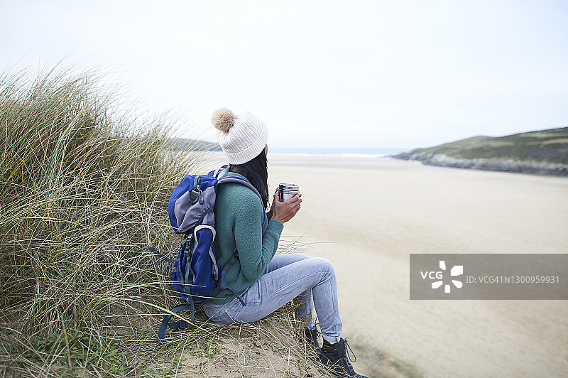 坐在海滩上喝着热饮，眺望大海的女徒步者图片素材