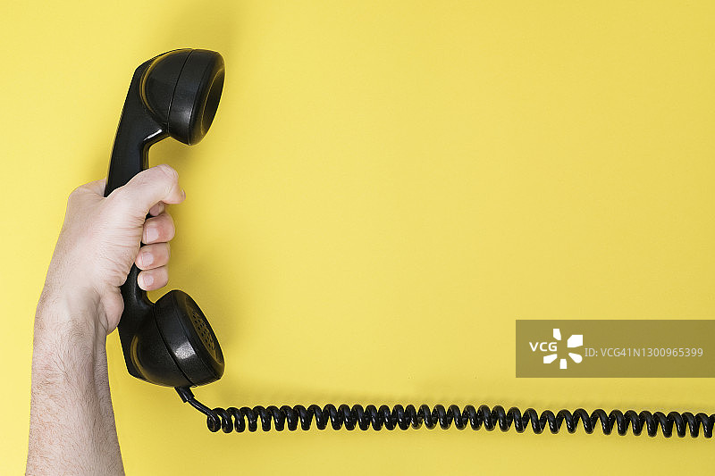 男人手持黄色背景上老式黑色电话的内部通讯装置的特写图片素材