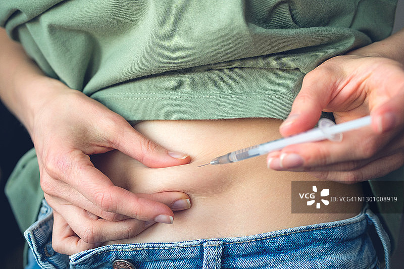 一位患有糖尿病的女人拉起腹部皮肤，用一次性注射器和小针头注射胰岛素，或者一位计划怀孕的女孩在人工授精或受孕前刺激排卵图片素材