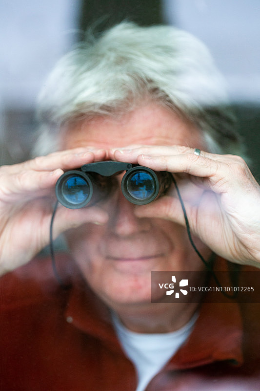 在窗边用双筒望远镜观察的年长男人图片素材