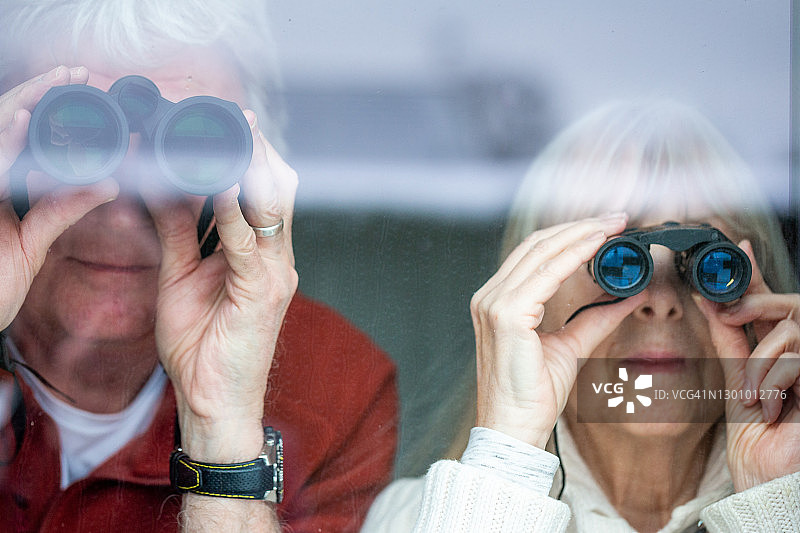 老年夫妇一起在窗边用双筒望远镜图片素材