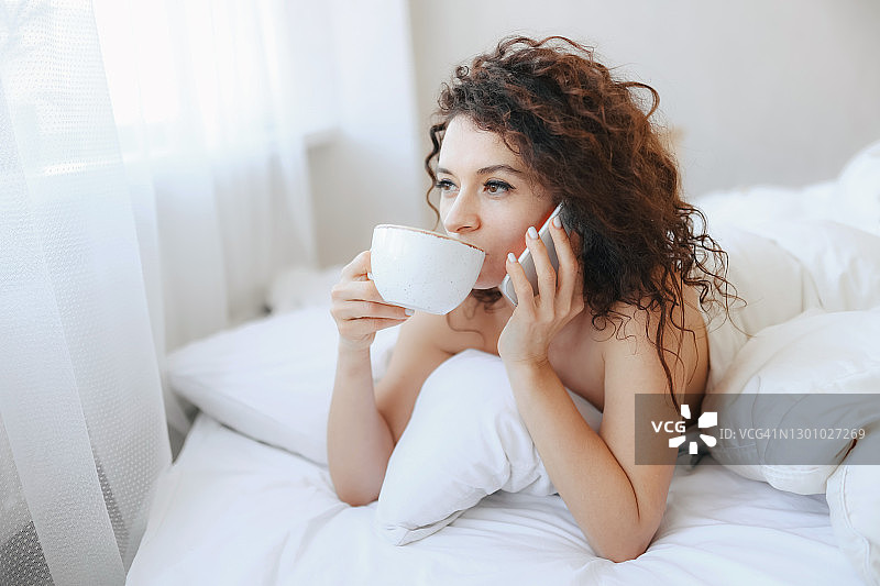 女人在床上喝咖啡并打电话图片素材