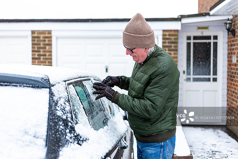 冬天成年男人在给被雪覆盖的汽车除冰图片素材