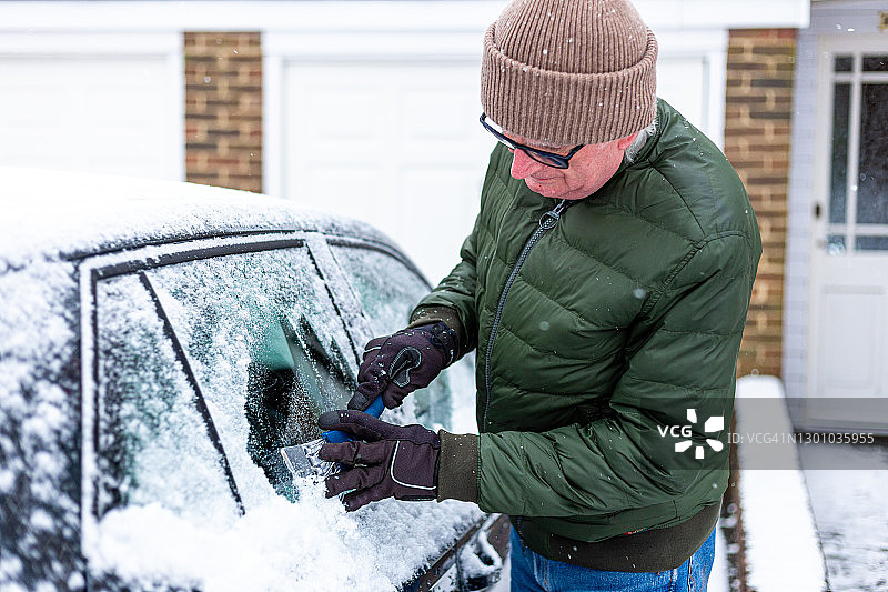 冬天成年男人在给被雪覆盖的汽车除冰图片素材