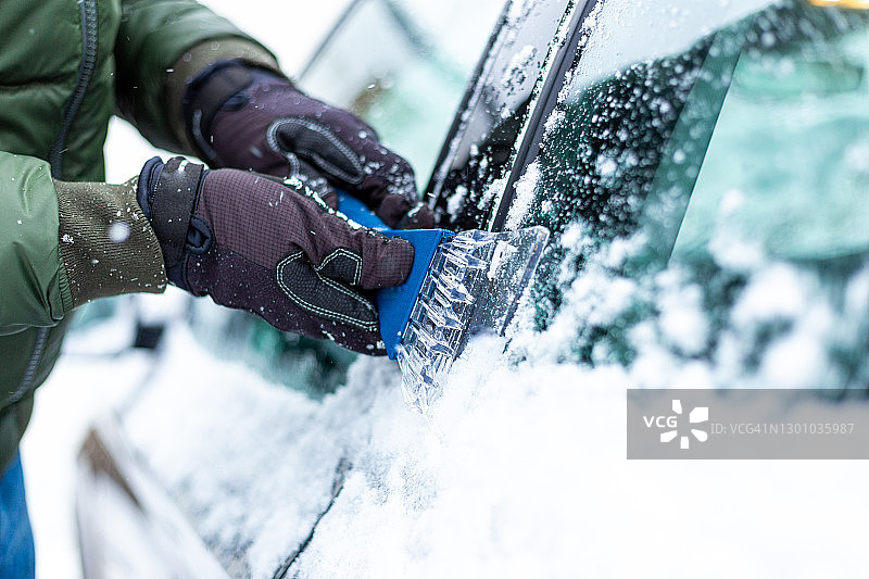 冬天成年男人在给被雪覆盖的汽车除冰图片素材