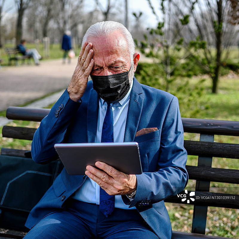 在公园长椅上使用平板电脑的年长商人图片素材