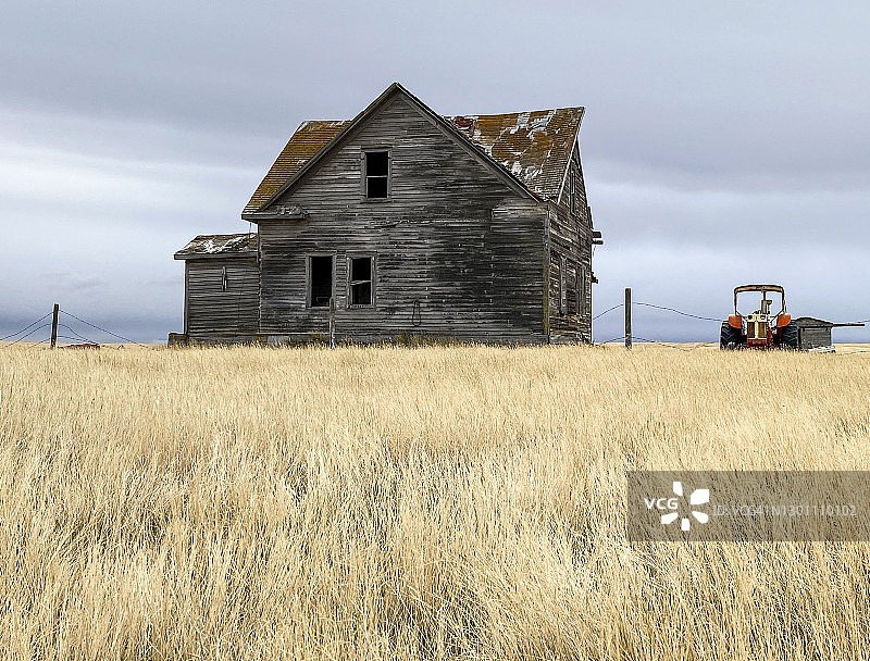 加拿大草原上，腐烂的农舍旁废弃的旧拖拉机图片素材