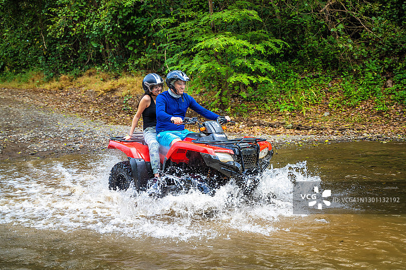 父亲和女儿在哥斯达黎加驾驶四驱摩托车过小溪图片素材