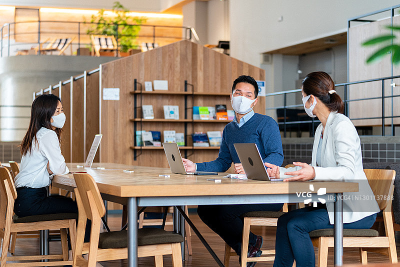 三位同事在现代办公室进行保持社交距离的会议图片素材