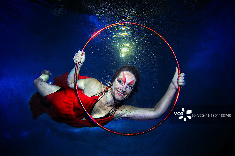 水下马戏团：模特在泳池中摆姿势，穿着红色衣服，化着浓妆，拿着呼啦圈图片素材