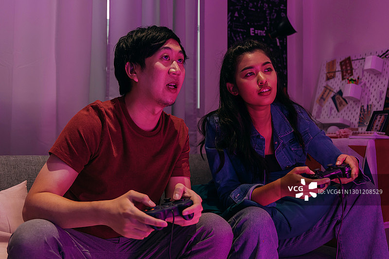 专注的亚洲女人和男人在沙发上玩电子游戏图片素材