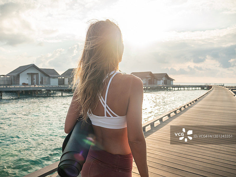 瑜伽老师在日出时前往木制码头瑜伽课的后视图图片素材