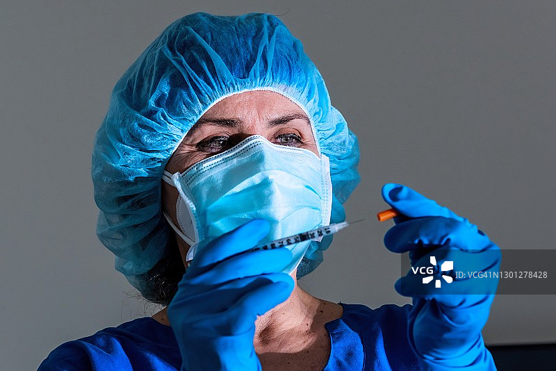 过度劳累的成熟女性医护人员拿着装有COVID-19疫苗的注射器图片素材
