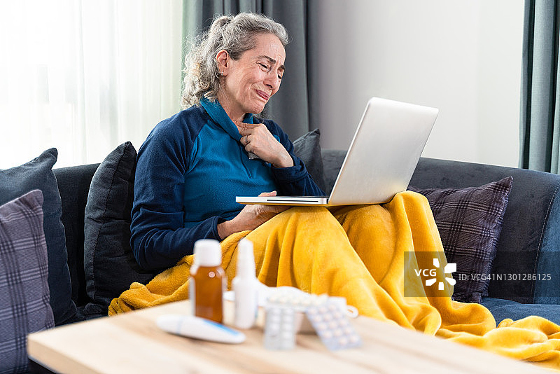 在家躺在毯子下，嗓子疼，向通过互联网联系的医生寻求帮助的中年妇女图片素材