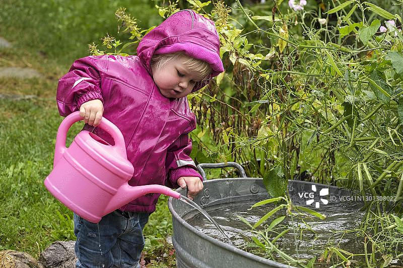 在德国巴伐利亚上巴伐利亚，穿雨衣和橡胶靴玩水和浇水壶的小女孩图片素材