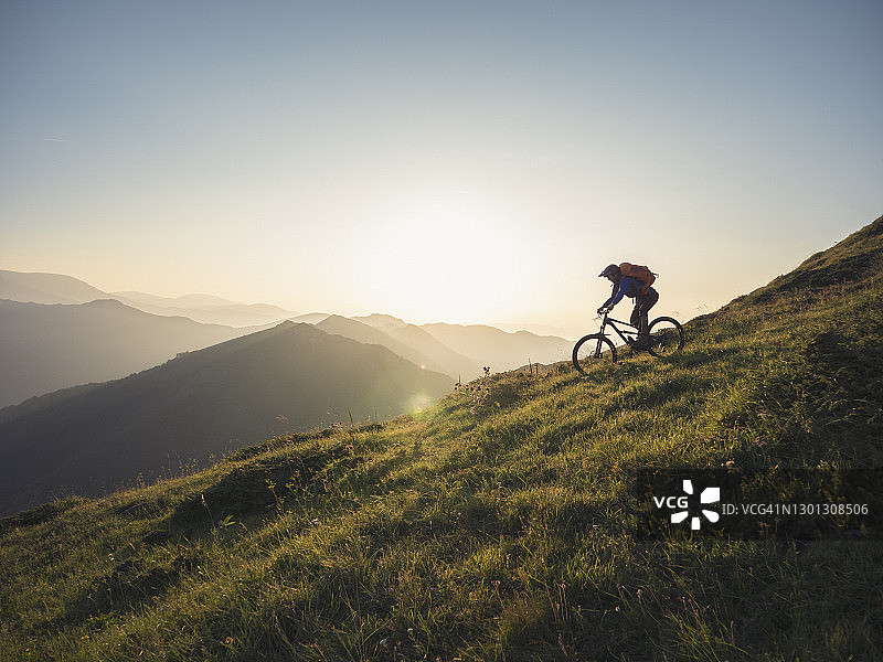 山地自行车手在日落时沿着山脊线骑行图片素材