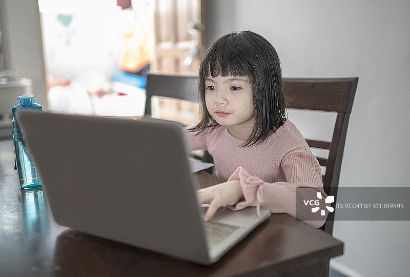 中国小女孩独自在厨房餐桌旁上网课图片素材