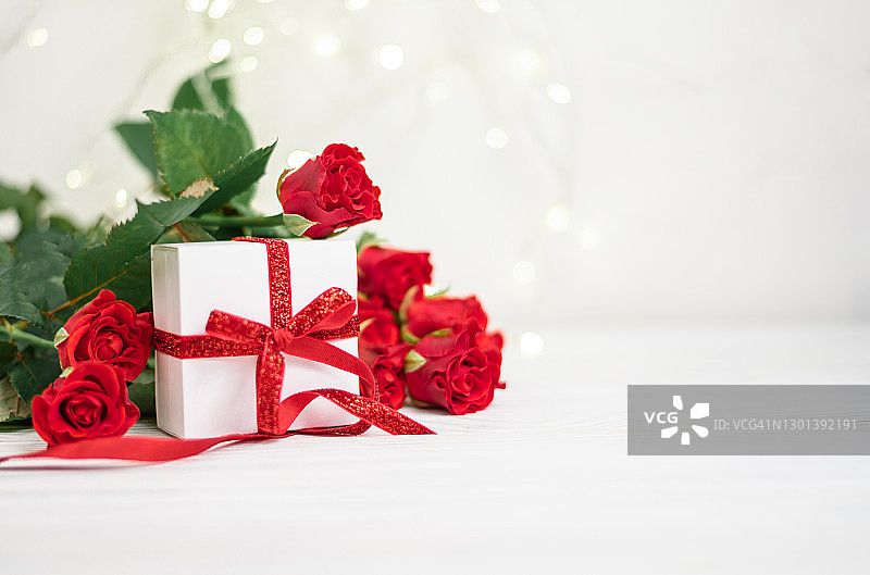 红玫瑰和散景背景上的红色蝴蝶结白色礼品盒，情人节母亲节三八节图片素材