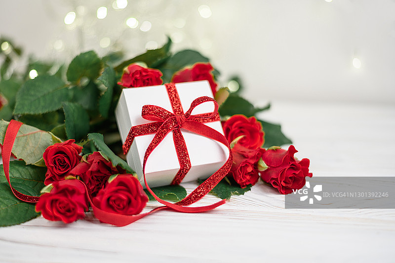 红玫瑰和散景背景上的红色蝴蝶结白色礼品盒，情人节母亲节三八节图片素材