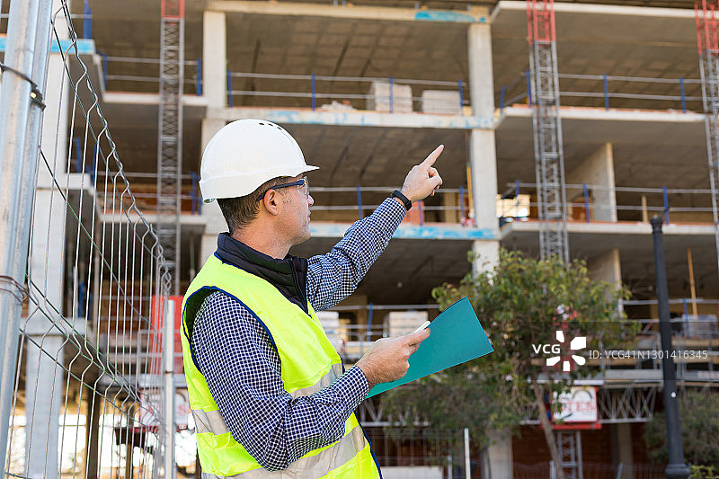 建筑工程师戴安全帽和反光背心，在建筑工地评估数据图片素材