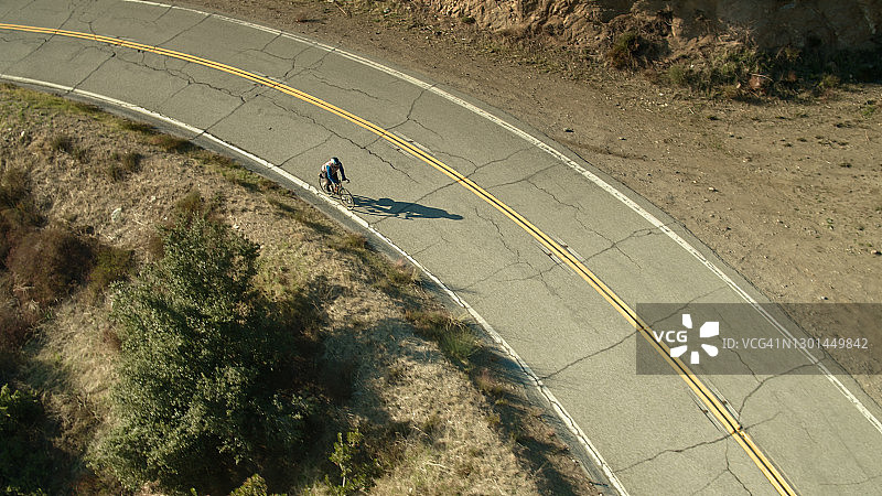 蜿蜒道路上骑自行车者的无人机拍摄图片素材