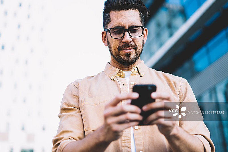 戴眼镜的白人男博主在户外使用智能手机和4G网络撰写邮件，阅读社交网络新闻图片素材