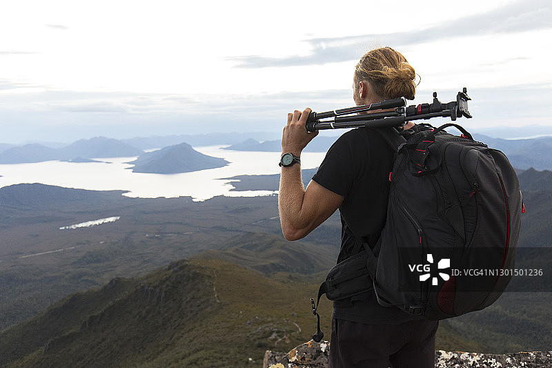 年轻男摄影师背着背包和三脚架眺望群山图片素材