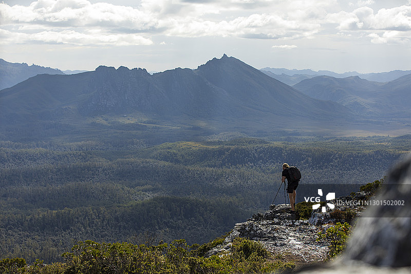 站在悬崖边拍摄山景的年轻男摄影师图片素材