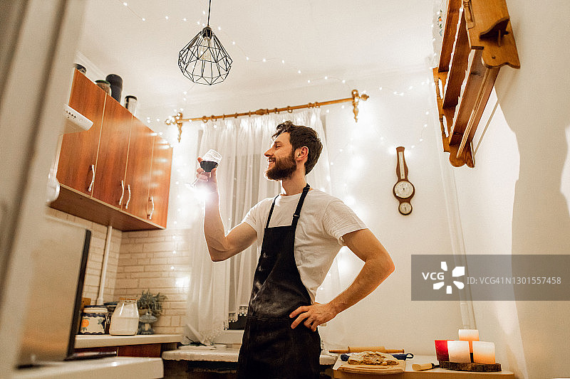 一位年轻男子在厨房做饭时拿着一杯葡萄酒图片素材