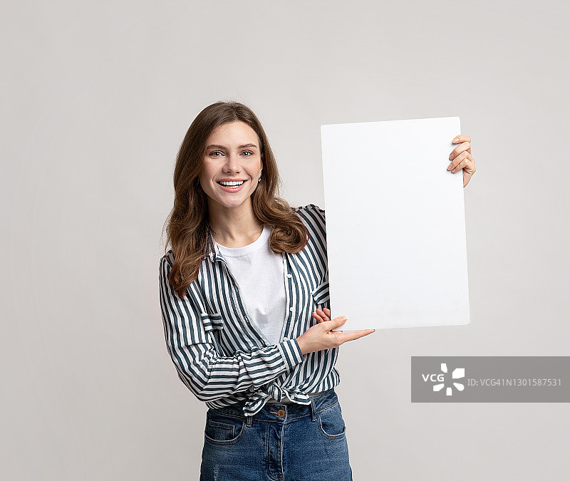 手持空白标语牌站在灰色背景前的快乐年轻女子图片素材