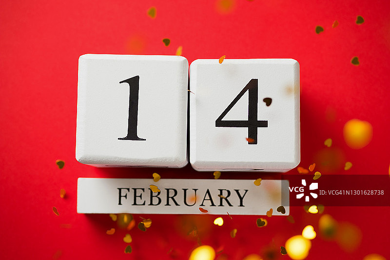 2月14日日历，白色木质日历上的铭文，红色背景。情人节贺卡。金色明亮闪亮五彩纸屑呈心形从上方飞落。浪漫构图。美丽的背景。图片素材