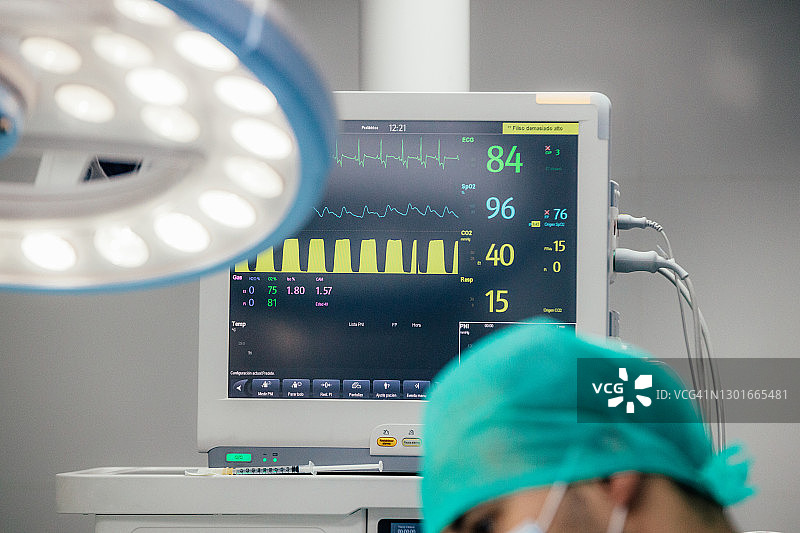 手术室内的医生特写，背景有心脏监护仪图片素材