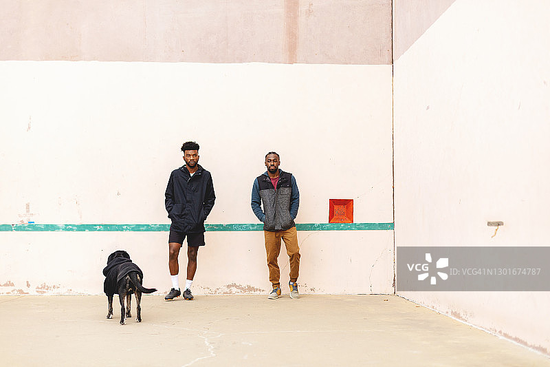 两名Gen Z男性在手球场上与宠物狗玩耍图片素材