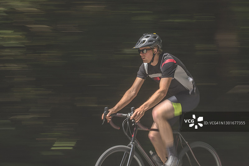 清晨，年轻男子骑公路自行车穿过绿色森林图片素材
