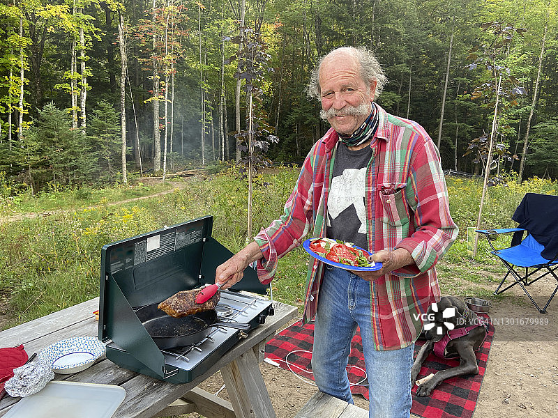 男子烧烤牛排在户外燃气烧烤野餐桌上图片素材