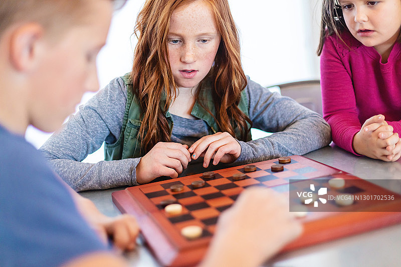 餐桌旁一起玩跳棋的三个孩子照片图片素材