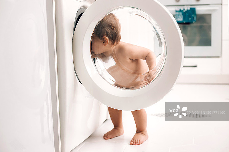 站在厨房洗衣机旁的可爱婴儿图片素材