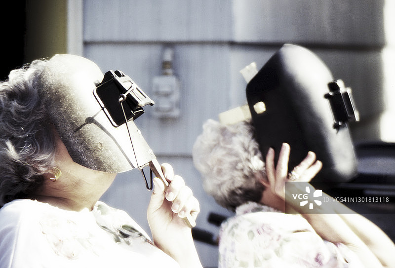 年长的妇女使用焊接面罩观看日食图片素材