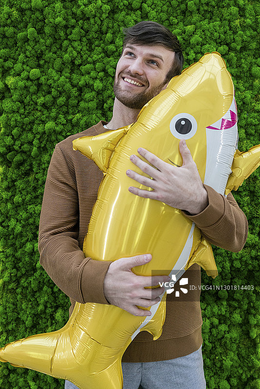 面带微笑的男企业家拿着充气鲨鱼，在绿色背景前做白日梦图片素材
