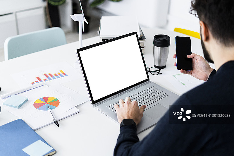 年轻商人在创意办公室使用笔记本电脑和智能手机图片素材