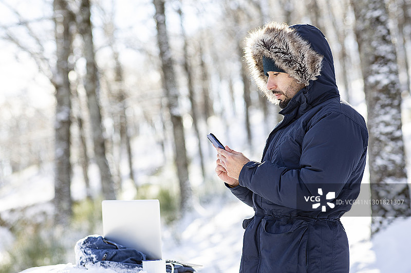穿着保暖的男人在雪中使用智能手机图片素材