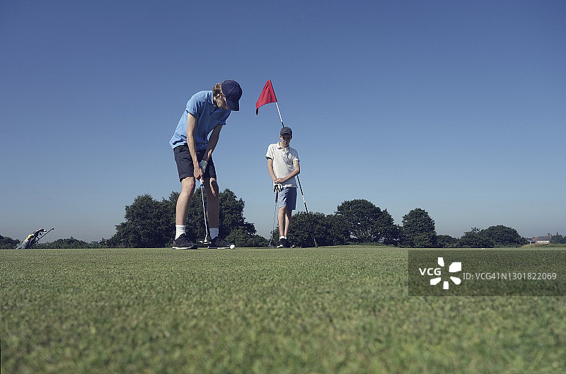 朋友们在球场上以蔚蓝天空为背景打高尔夫图片素材